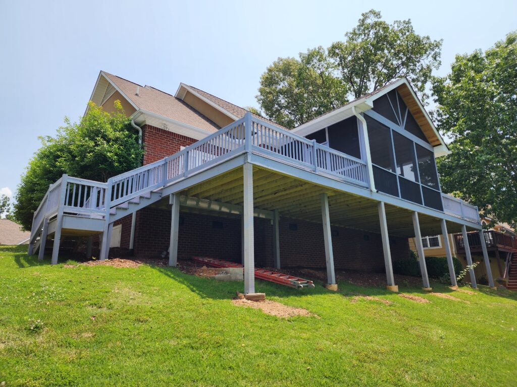 New deck and stairs addition to large house with screened in porch and grass in the foreground