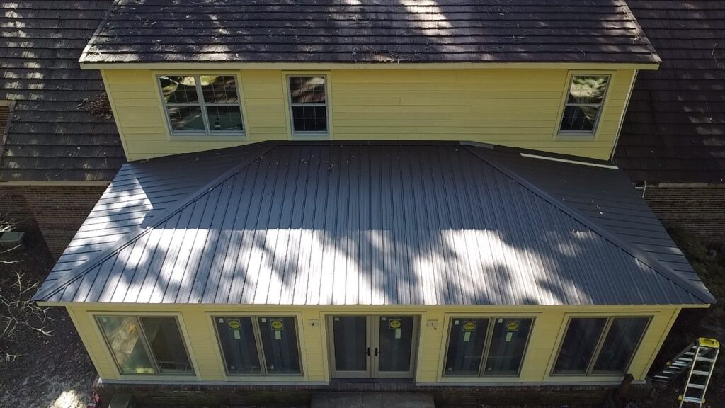 New gray metal roof over a sunroom addition beneath an existing shingle roof